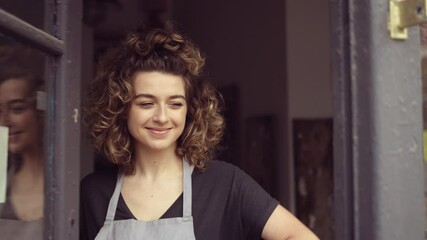 Wall Mural - Smiling young woman at the door of her shop welcoming customers 
