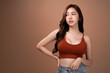 © AtidChalermsong - Slim body and big breast asian woman looking and arms akimbo, Red crop bralette outfit, isolated with mocha brown background