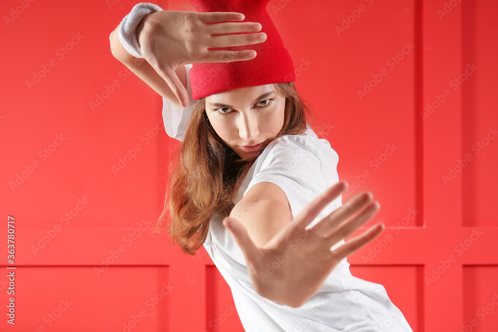 Beautiful female hip-hop dancer against color wall