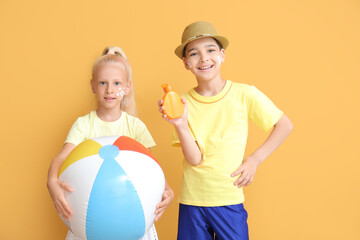 Wall Mural - Little children with sun protection cream and inflatable ball on color background