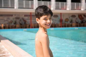 Wall Mural - Little boy with sun protection cream on his body near swimming pool