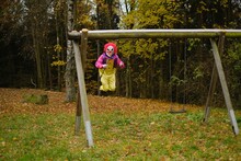 Halloween Holiday Concept. Spooky Clown On A Swing In The Autumn Forest