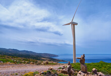 Single Windmill Turbine, Road And Balancing Stones On Hilltop Of Seashore In Colorful Landscape At Dynamic Blue Sky On Clear Sunny Summer Day.