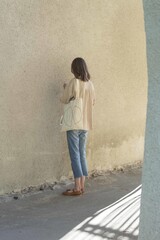 Poster - Vertical shot of a female with a white-colored tote bag standing while facing a wall