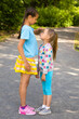 © zabavna - Two little sisters are measuring their growth outdoors in summer park. Elder girl comparing their height by her palm