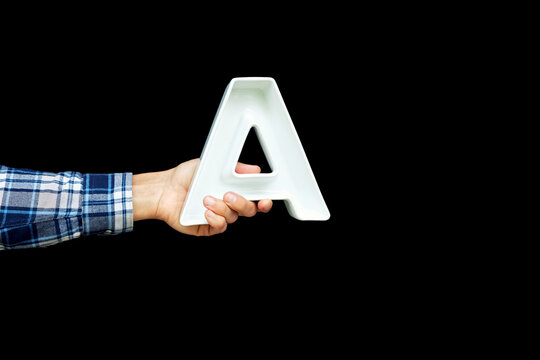 Person hand holding large voluminous letter A on black background. Back to school, education concept.