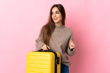 Young caucasian woman isolated on pink background in vacation with travel suitcase