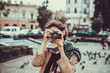 © Andrii - Young female tourist visiting old town on vacation and taking photos on old camera on the street.