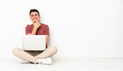 Teenager man sitting on the flor with his laptop smiling