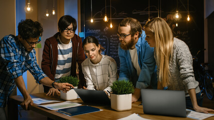 Wall Mural - Late at Night Team of Young Creative Developers Have Brainstorming Session at their Meeting Table, Use Laptop, Discuss Ideas and New Concepts. Stylish People in Trendy Office Environment.