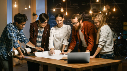 Poster - Late at Night Team of Young Creative Developers at their Meeting Table Spread Blueprint and Get Down to Work. Stylish People in Trendy Office Environment.