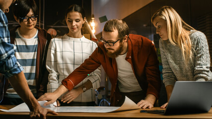 Poster - Late at Night Team of Young Creative Developers at their Meeting Table Spread Blueprint and Get Down to Work. Stylish People in Trendy Office Environment.
