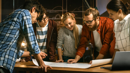 Poster - Late at Night Team of Young Creative Developers at their Meeting Table Spread Blueprint and Get Down to Work. Stylish People in Trendy Office Environment.
