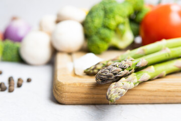 Group of organic fresh vegetables - green asparagus, broccoli, mushrooms on grey background, flat lay. Concept of  healthy vegetarian food, diet and home cooking.