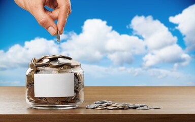 Wall Mural - Hand putting coins in a glass jar with a blank label