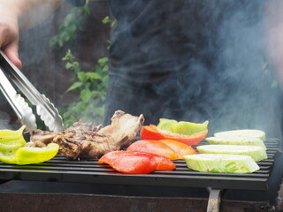 the cook turns vegetables with meat tongs on the grill on the coals. delicious food.