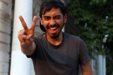 Young Man winking and smiling while showing peace sign with his fingers.