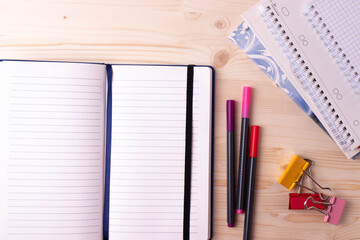 various pens and a pile of notebooks on the wooden backgrounds