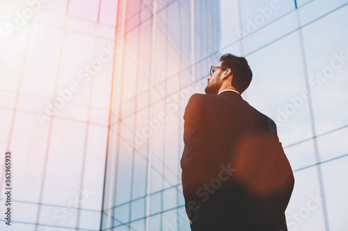 Photographie Back view of serious businessman in eye glasses looking on copy space while stan