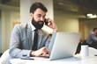 © BullRun - Confident bearded male HR manager of IT corporation making phone call to banking service confirming money transfer while paying on website, professional HR manager making job offer contact on mobile