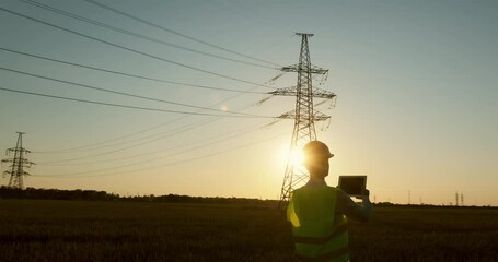 Wall Mural - a power worker inspects high-voltage power lines at sunset using a tablet.
