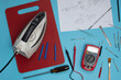 © Cautivante.co - Clothes iron for repair accompanied by multimeter and assembly plan of the piece. home appliance repair concept. Electronic technician table with blue service background.