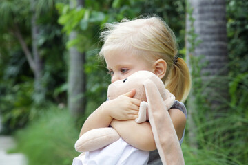 Outdoor portrait of cute 3 years old girl hugging plush toy. Close up image of child and stuffed animal rabbit toy.