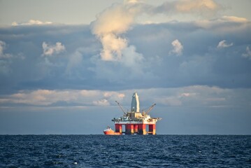 Drilling platform at sea. Extraction of minerals on the shelf. A huge red platform rises above the water. The ship is nearby. Hydrocarbon energy. 