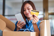 © Farknot Architect - Closeup image of a beautiful young woman using mobile phone and credit card for online shopping with shopping bag and postal parcel box of clothing on the table