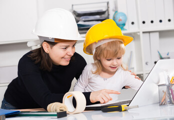 Female with child are sitting in helmets and looking in laptop at the home.