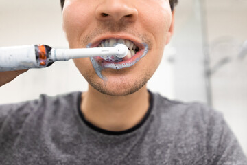 Man with electrical toothbrush brush his teeth with toothpaste on his mouth