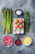 Asparagus with eggs and french dressing ingredients with dijon mustard, onion chopped in red vinegar  taragon on grey textured background, top view.