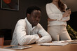 © Anatoliy Karlyuk - Successful experienced Afro American CEO sitting at office desk studying financial report made by his young female assistant. Multi ethnic team of black man and white woman working together