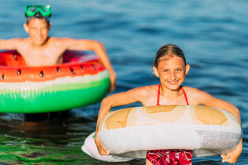 Wall Mural - children boy and girl, swimming in the sea with inflatable circles, having fun on the beach during the summer holidays