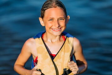 Wall Mural - Happy beautiful little girl in a life jacket, swimming in the sea and showing a winning gesture. Summer holiday, vacation