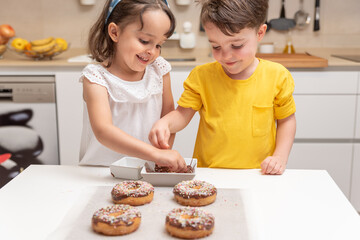 Children decorating doughnuts with colorful sprinkles at home