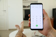 © Thomas - A hand holding a new cellphone, which displays the numeric dial pad on the touch screen. In the background, the legs of the person who's sitting in