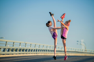 Two teenage girls perform an acrobatic element outdoors against a blue sky	