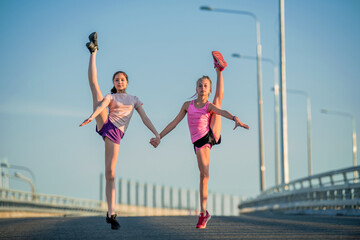 two teenage girls perform an acrobatic element outdoors against a blue sky