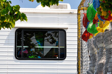 Window Of An RV Near A Fairground Midway, With Plush Game Prizes Reflected In The Window.
