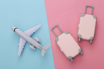 Two toy travel luggage and air plane on pink blue pastel background. Travel planning. Top view. Flat lay