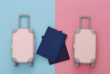 Two toy travel luggage and passport on pink blue pastel background. Travel planning. Top view. Flat lay