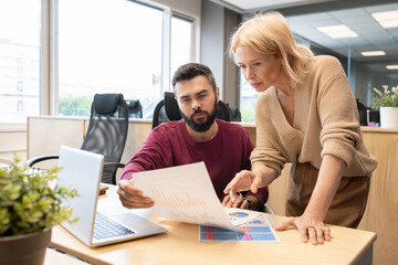 Leinwandbilder - Blond mature businesswoman pointing at financial paper held by young colleague