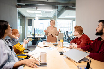 Leinwandbilder - Mature woman standing by table in front of her young intercultural colleagues