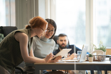 Poster - Young Asian businesswoman and her Caucasian colleague looking at tablet display
