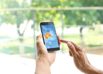 Wall Mural - man using weather forecast app on smartphone near window, closeup
