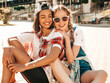 © halayalex - Two young smiling beautiful girls with colorful penny skateboards. Women in summer hipster clothes sitting in the street background. Positive models having fun and going crazy