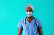 © Carlos David - Portrait of a young african male er doctor wearing mask for covid-19 corona virus protection against blue studio background