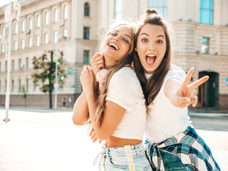 Portrait of two young beautiful smiling hipster girls in trendy summer white t-shirt clothes.Sexy carefree women posing on street background. Positive models having fun and hugging