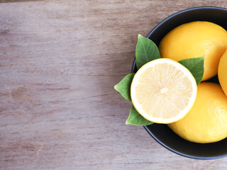 Half and group of fresh lemon with leaves in black bowl on wooden background. Copy space for text. High Vitamin C, view from above.